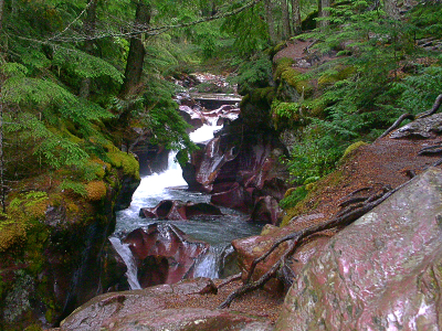 [Through a small thin canyon composed of red rock, the water drops several times with pooling sections between the drops. Lots of whitewater and lots of greenery on the tops of the rocks.]